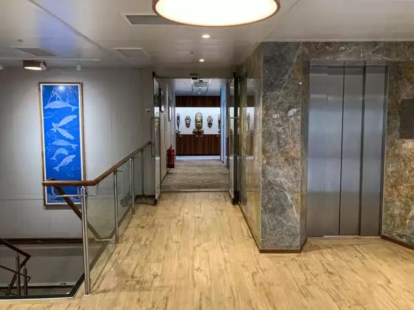 Elevator aboard Coral Adventurer, light wooden floor with stone granite walls and a silver metal elevator