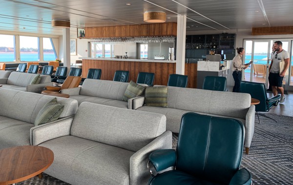 Lounge area of Coral Adventurer, grey love seats with dark teal leather chairs
