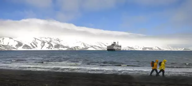 Small expedition ship in Antarctica with guests walking on land.