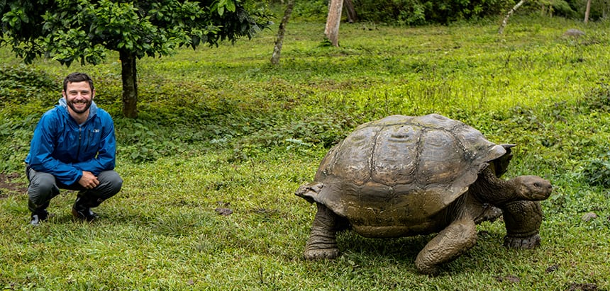 Green lush landscape with galapagos tortoise and traveler kneeling next to it
