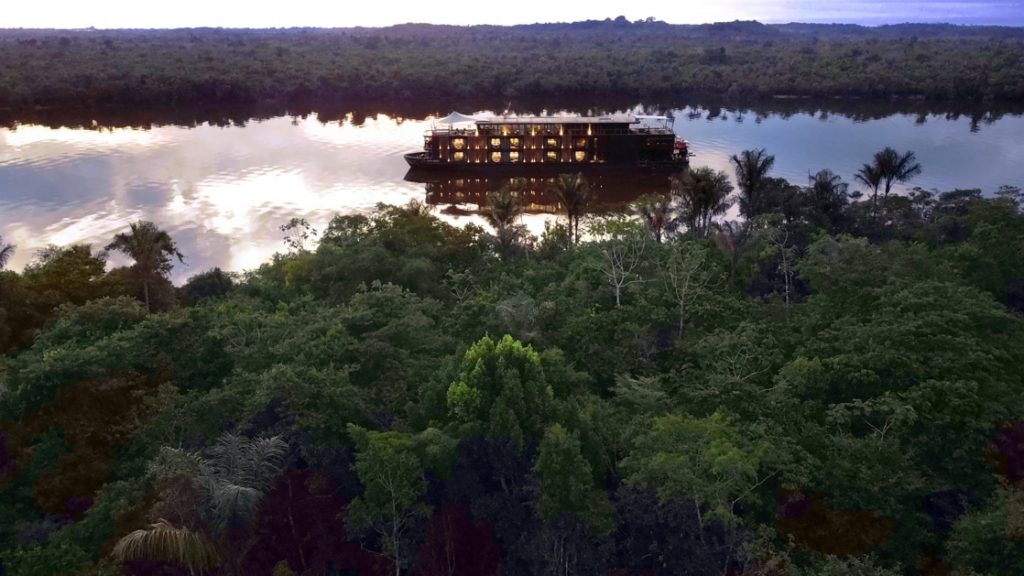 It's nightfall in Peruvian Amazon jungle, the luxury Aqua Nera cruises down the river windows glowing from lights inside.