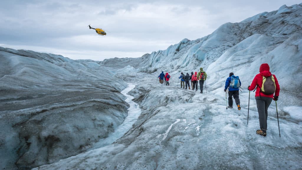 Glacier hikers on the icecap near Kangerlussuaq, with a helicopter in the sky, during the Greenland Adventure cruise by land, sea and air.