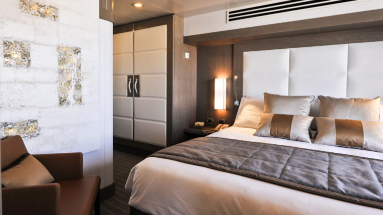 owners suite aboard Le Boreal luxury expedition ship, white leather headboard a closet and a seating area