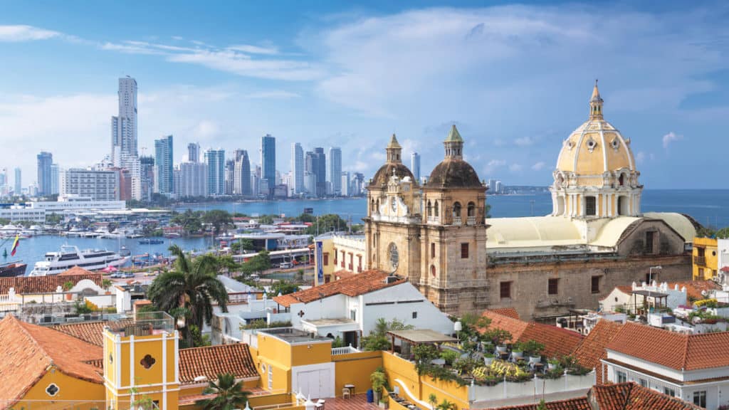 Aerial view of Cartagena, Colombia, with modern high-rise buildings and colorful Caribbean buildings including a church.