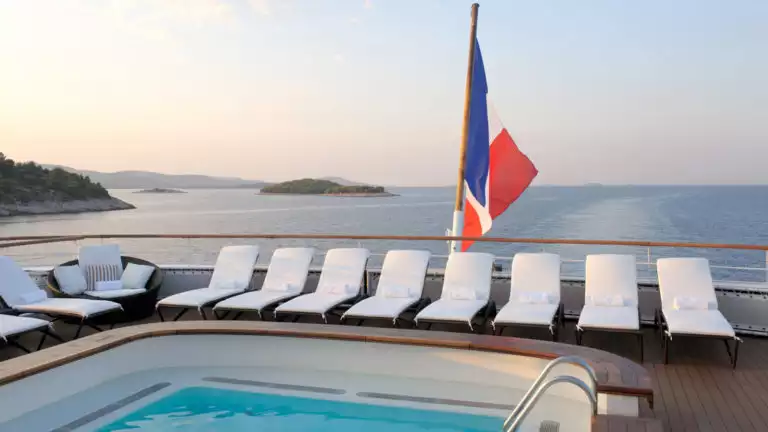 pool on small cruise ship overlooking sunset skis and calm waters with many white lounge chairs set next to the pool.