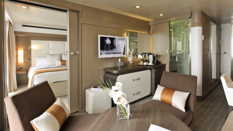 Prestige Suite for Decks 4, 5 & 6 aboard L'Austral expedition ship, showing king bed, table, TV, chairs & white-&-copper appointments.