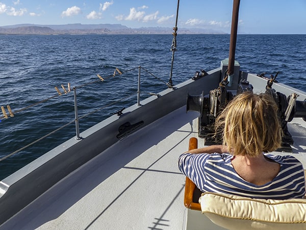 A single female traveler sits on the bow of a small ship in Baja