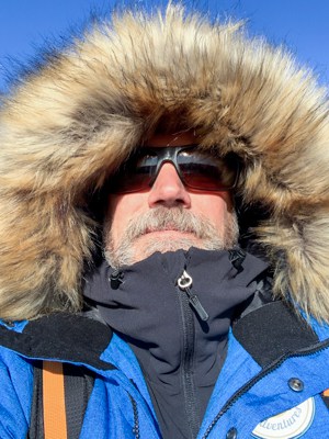 A portrait of Todd Smith founder of AdventureSmith Explorations on the Classic Polar Bear Adventure tour, he is wearing a royal blue jacket with a hood up around his head covered in fur