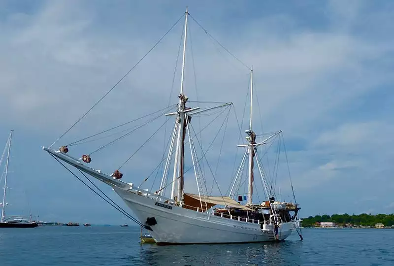 the all white indonesia small ship katharina floats in the ocean, its long wooden bow reaches out