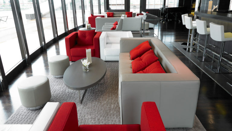 lounge seating aboard Le Boreal, grey couches with red pillows, red arm chairs and coffee tables in front of tall glass wrap around windows