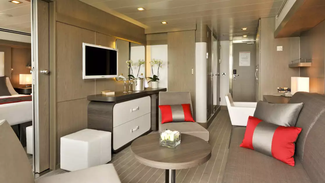 Prestige Suite for Decks 4, 5 & 6 aboard Le Boreal expedition ship, showing king bed, table, TV, chairs & white-&-copper appointments.