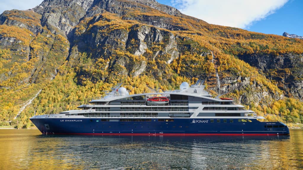 Le Champlain, luxury expedition ship with a red, blue & white exterior, sits in front of cascading waterfalls.