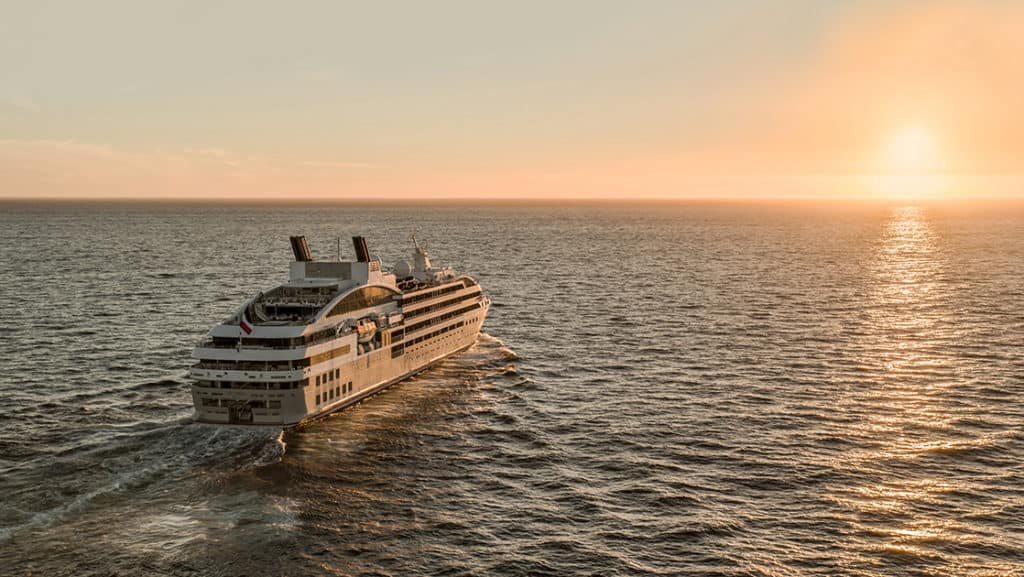 Luxury French ship Le Lyrial cruises toward the sunset, out at sea.