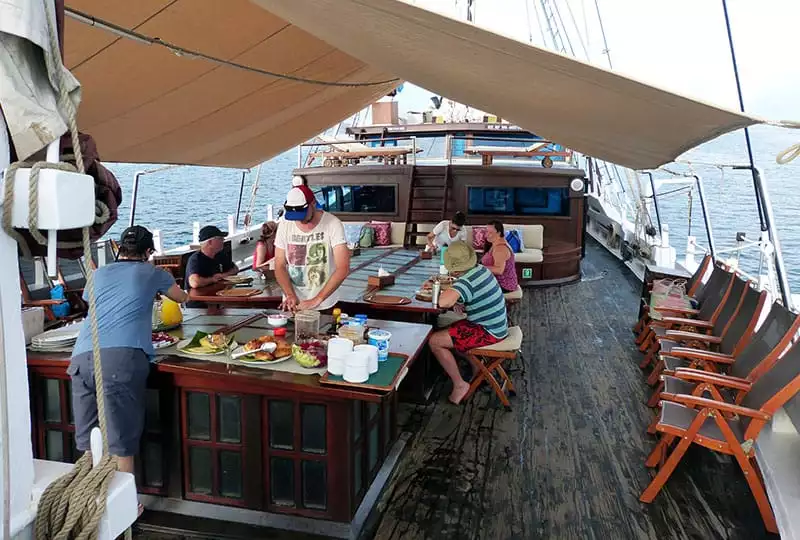 the cruise guests gather around an outdoor but covered dining area on the stern of the ombak putih, some are in line getting food from the buffet line