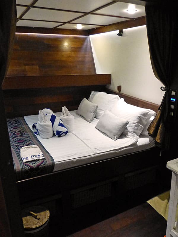 a single cabin with a double bed aboard the ombak putih, dark wood walls with white bedding