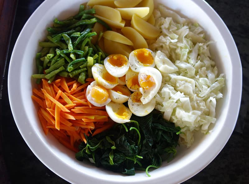 a bowl of indonesia soup, carrots, eggs, green onions, sprouts and broth are inside