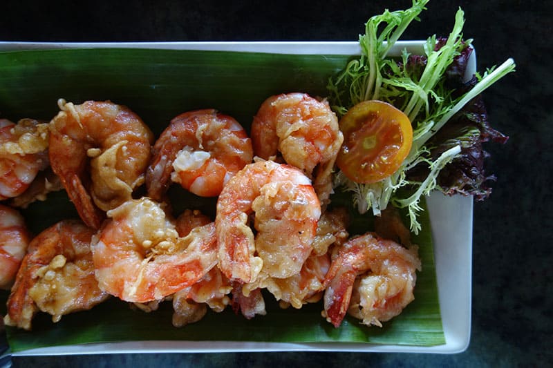 a plate of fried shrimp with a small salad of greens and tomato