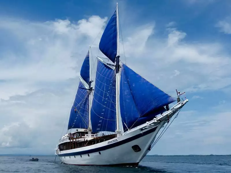 indonesia cruise small ship ombak putih, front view with blue sails up against blue ocean and blue sky