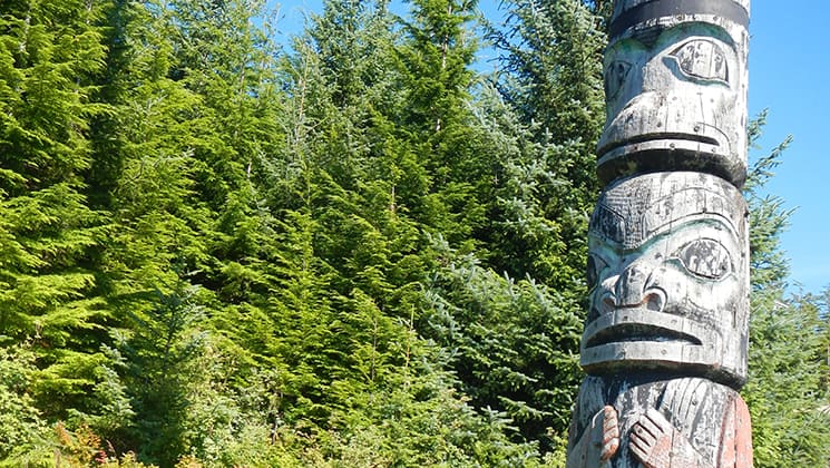 Totem pole on a sunny day beside thick green forest reveals indigenous culture on the Remote Alaska Adventure small ship cruise.