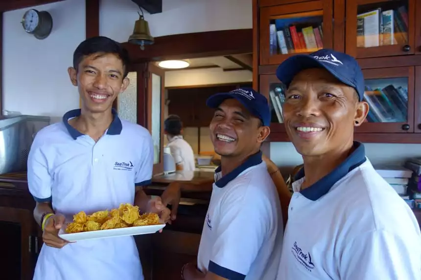 Three Indonesian ship crew members smile for the camera in their uniforms, one is holding a tray of food