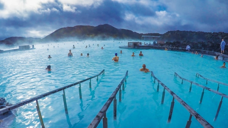 Railings lead into the turquoise blue waters of the Blue Lagoon with steam rising and people bathing, during the Wild Iceland Escape arctic cruise.