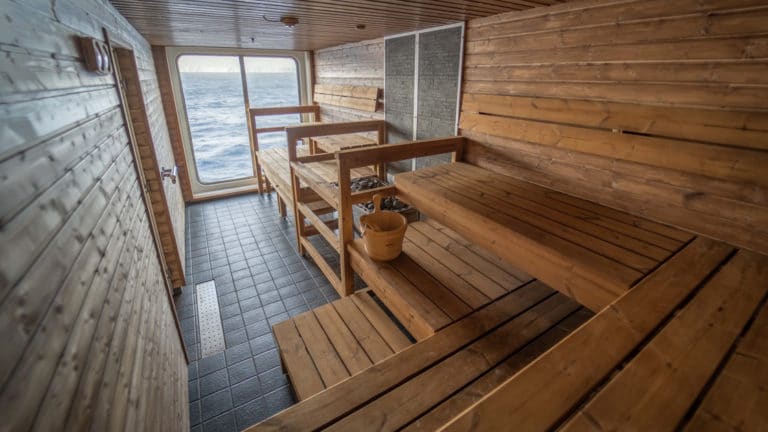 Wooden sauna with 2 seating rows, hot rocks & picture window aboard Greg Mortimer polar ship.