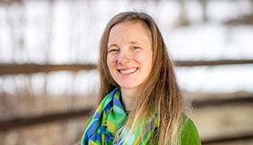 adventuresmith explorations content manager mary kohut wearing bright green and blue smiles standing in front of a fence