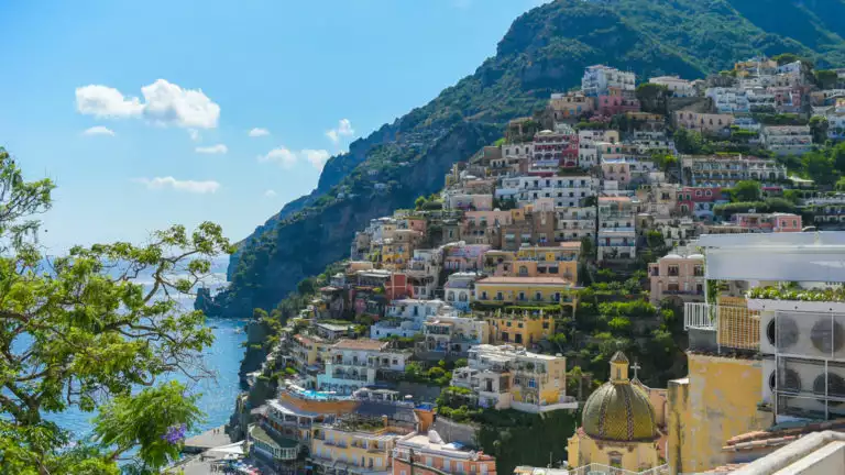 The town of Amalfi, Italy, rises upward from turquoise water along the hillside, with colorful buildings & a church, seen on the Best of Croatia Cruise.