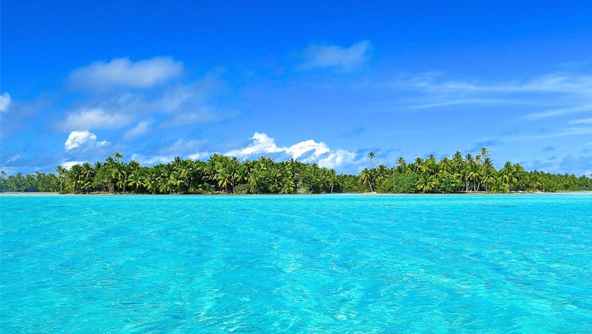 crystal clear teal water split from the blue sku with a lush palm tree filled island in French polynesia. 