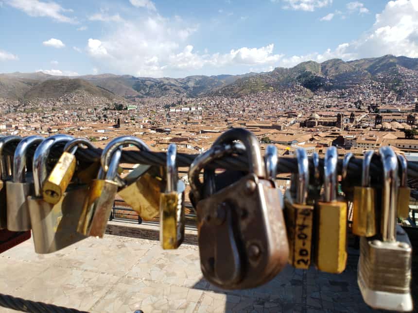 A row of locks hang from a wire bridge in front of of a landscape view of Cusco, seen before departing on a Machu Picchu land tour.