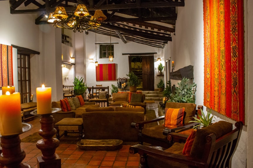 The inside of Inkaterra Machu Picchu hotel during a Peru land tour. Warm orange red and yellow wall hanging decor and candles fill the room with comfy arm chairs and love seats