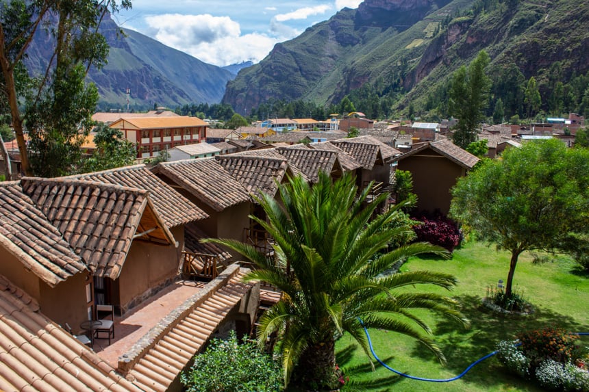 The grounds of Lamay Lodge inside Sacred Valley, Peru. Adoble shingles on top of many roofs are pictured as the lodge sits infront of a lush green mountain range.