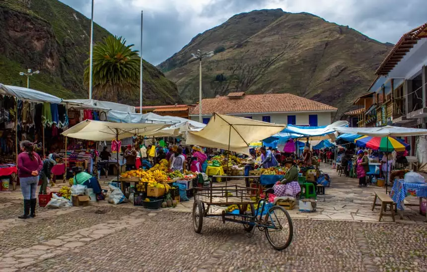 An outdoor market in the Sacred Valley of Peru. Umbrellas stand over tables filled with fruits, crafts, clothes and more. All seen as part of a Machu Picchu land tour.