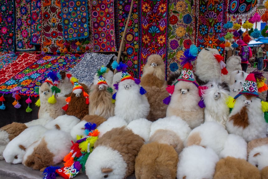 A brightly colored market table filled with plush Llama toys and woven table runners in the Sacred Valley, Peru.