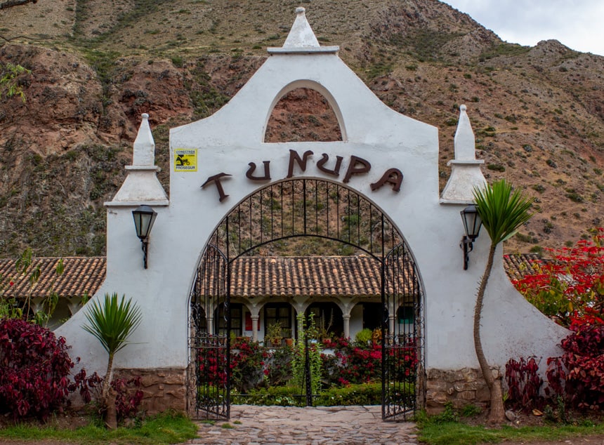 The entry way of Tunupa hotel in the Sacred Valley, Peru. Bright white stone arch with a black gate open to the hotel that sits in front of a dessert like hillside.