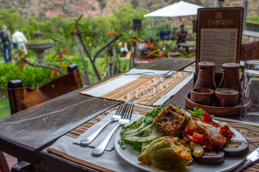 A full plate of varied food set on a table seated outdoors in a lush green garden of a hotel in the Sacred Valley Peru.