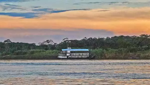 A small riverboat cruise ship is seen near the shore of the Amazon River in Peru at sunset