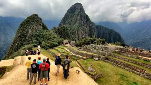 A small guided group gathers on a dirt path in the foreground of the Machu Picchu ruins and the towering Huayna Picchu