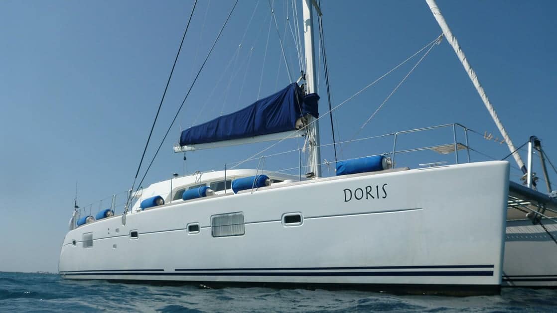 Exterior of the Belize charter ship Doris, all white with royal blue sails, she sits on the ocean on a clear blue sky day