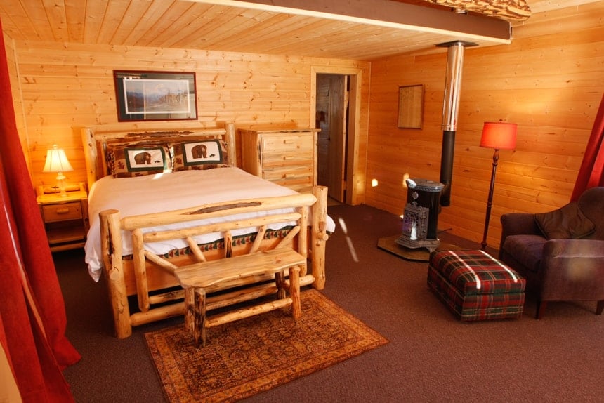 Inside the rustic cabin at Winterlake lodge, wood log walls, with a wood burning stove and a kind side bed