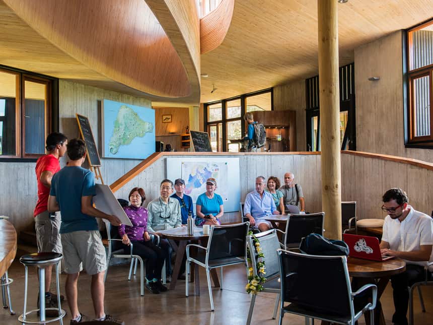 a group of travlers sit in the lounge of Explora Rapa Nui Lodge, they lsiten to their guides discuss the days activities