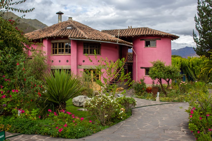 Pink clay buidling at Sol Y Luna, a lodge in Peru's Sacred valley, a stone walk way winds betwwen green grass and colorful flower beds