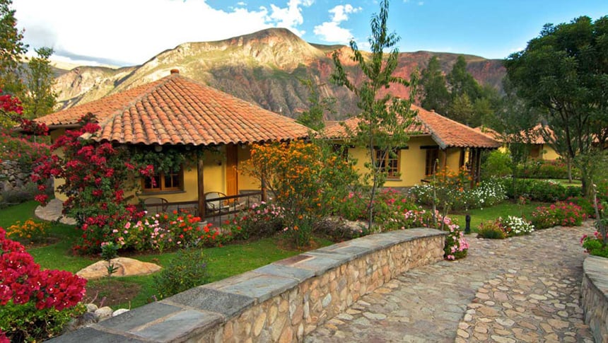 Yellow clay buidlings at Sol Y Luna, a lodge in Peru's Sacred valley, a stone walk way winds betwwen green grass and colorful flower beds