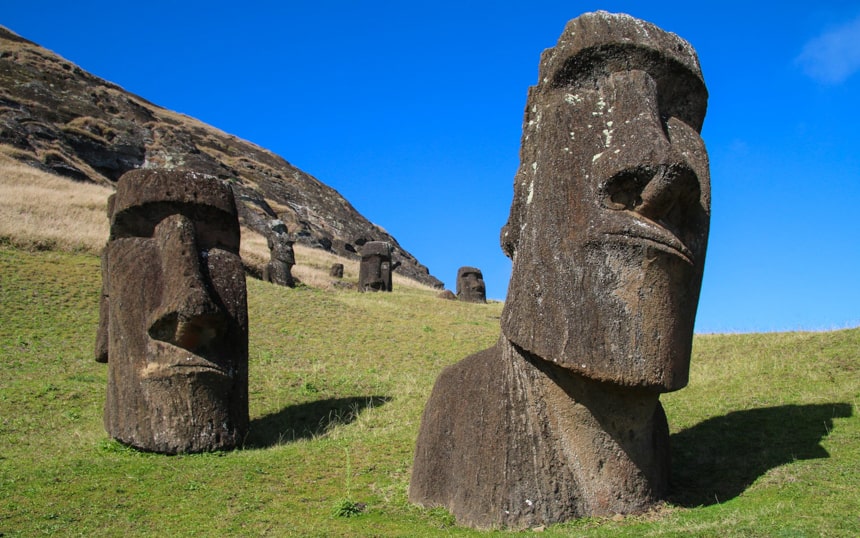 stone sculpures of faces on Easter Island sit on green hiullside ifnron of a blue sky, seen while staying at Explora Rapa Nui Lodge