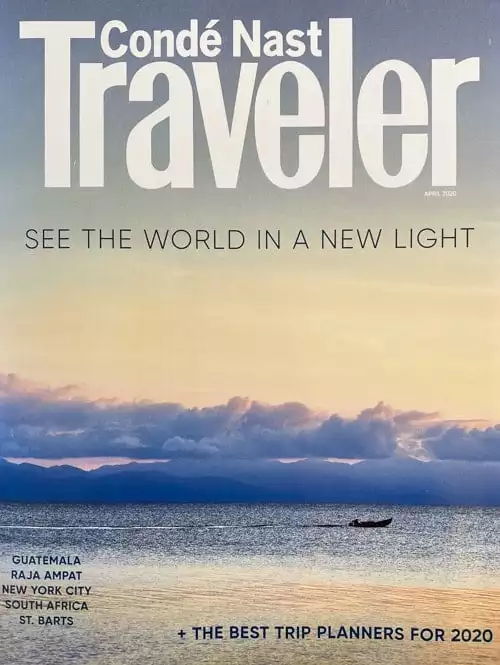 Cover of the April 2020 issue of Conde Nast Traveler magazine. A Peach sunset with purple clouds reflect on a body of water with a small man powered boat paddling. 