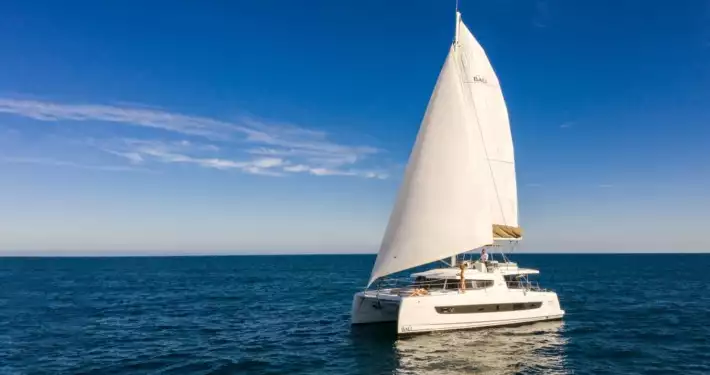 Belize charter yacht First Tracks, a 46-foot while catamaran, sits in calm water with both sails fully open.