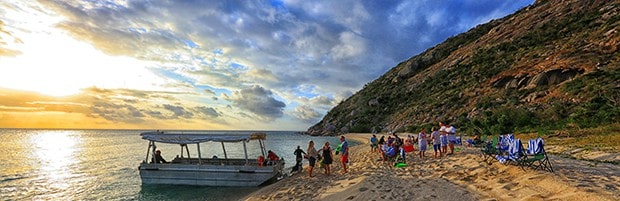 A group of people on the beach at sunset in Australia, with a ferry docked on the beach