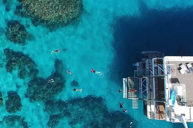 People snorkeling around a small ship above a reef in the Great Barrier Reef