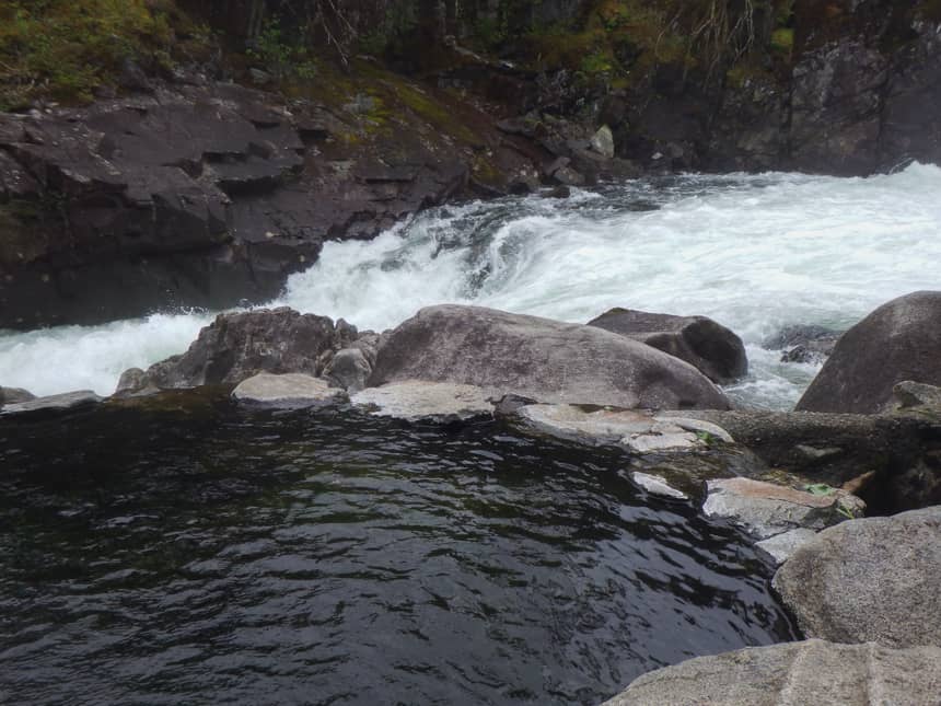 Baranof Warm Spring, a circular pool of water surrounded by rocks, sits against a rushing river, a group of cruise passengers visited on their Alaska small ship cruis