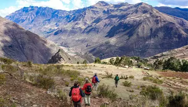 A group of hikers on a Peru trek down to Pisaq seen on a grassy hillside with big brown mountains in the background.